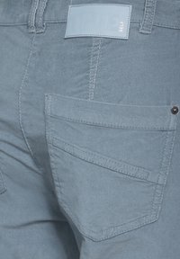 Lichtblauwe denimbroek met een gestructureerde afwerking, zichtbare stiksel en een merketiket op de tailleband. Achterzak met een knoopdetail.