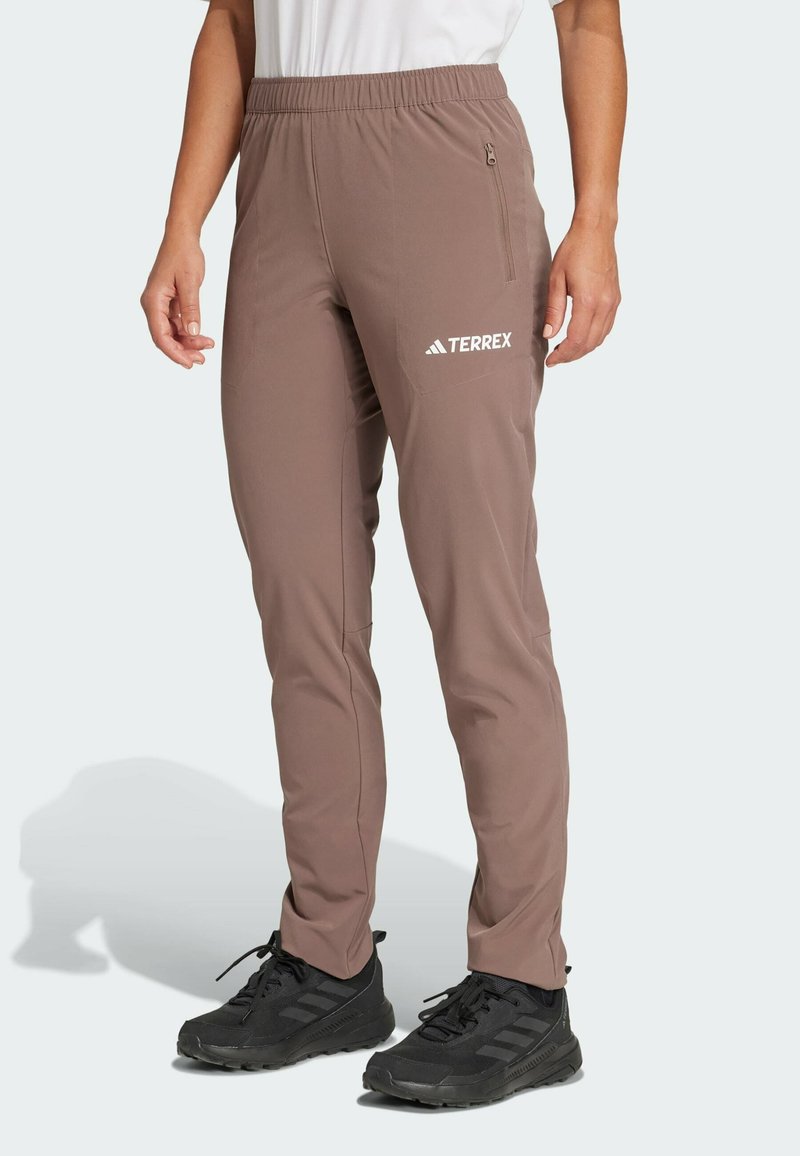 Brune, lette, strekkelige bukser med elastisk midje, sidelomme og hvit "TERREX"-logo på låret. Egnet for utendørsaktiviteter.