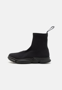 Botines tipo calcetín negros con un upper de textil suave, suela de goma gruesa y una pestaña en la parte trasera para facilitar su uso.