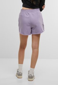Shorts di cotone lavanda con elastico in vita, caratterizzati da un bordo ondulato e un piccolo design ricamato sul lato sinistro.