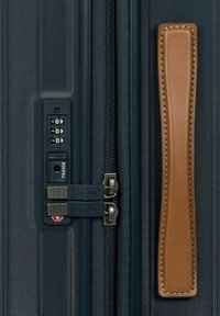 Valigia da viaggio con un'esterno testurizzato di colore blu scuro, doppie chiusure lampo, una serratura combinata e una maniglia in pelle beige.