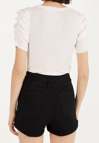 Vit ribbad topp med puffärmar, kombinerad med höga svarta shorts med en åtsittande passform och uppvikta ärmar.