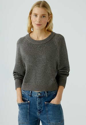 Grijze gebreide trui met een brede ribbelkraag en manchetten, gecombineerd met losse blauwe denim jeans met grote voorkruiszakken.