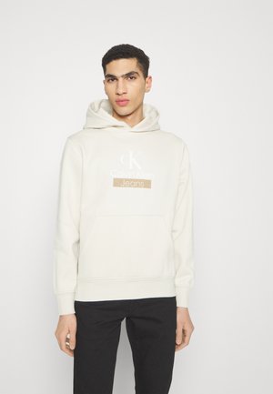 Felpa crema in cotone misto con tasca a marsupio, stampa del logo in bianco e caramello, polsini a coste e cappuccio con coulisse.