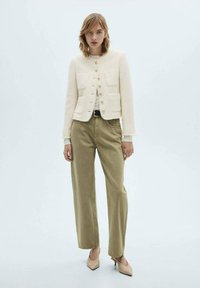 Cream tweed jacket with gold buttons and two front pockets, paired with wide-leg olive green pants and beige pointed-toe heels.