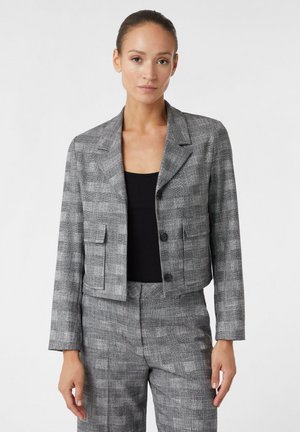 Blazer à carreaux gris coupé, avec des épaules structurées, des revers notch et deux poches avant. Porté sur un haut noir.