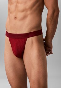 Roter Baumwolltanga mit geometrischem Muster, strukturiertem Stoff und einem Markenbund. Sitzt eng und betont die Körperkonturen.