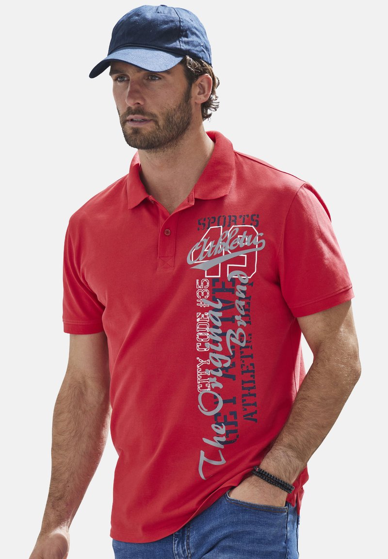 Rotes Poloshirt mit kurzen Ärmeln. Mit bedrucktem weißen und grauen Text. Aus weichem Baumwollmaterial. Kombiniert mit einer blauen Kappe.