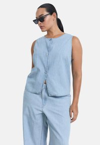 Light blue denim vest with sleeveless design, front button closure, and a straight cut. Smooth texture and minimal stitching details.