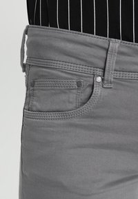 Jeans de mezclilla gris que presentan un bolsillo delantero, cinturilla cosida y detalles en botones metálicos. La textura parece suave, con un ligero estiramiento.