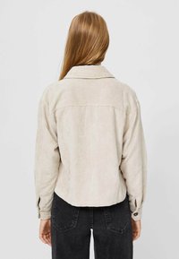 Beige corduroy jasje met een kraag, een drop-shoulder ontwerp en knoopdetails op de manchetten. Heeft een iets cropped silhouet en ribbeltextuur.