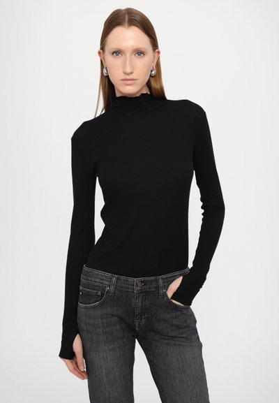 Črni dolg rokav turtleneck toplj z gladkim materialom, v kombinaciji s temno sivoh kavbojkami z rahlo uničenim videzom in sprednjimi žepi.