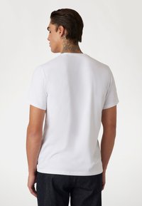 Camiseta de algodón blanca con cuello redondo y mangas cortas, mostrada desde la parte de atrás, con una textura suave y un corte relajado.