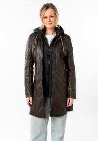 Manteau en cuir marron au design ajusté, doté d'une couche intérieure à capuche noir matelassée et amovible ainsi que de poches zippées. Texture lisse.