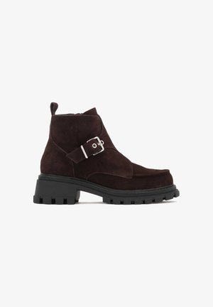 Bruine nubuck enkellaarzen met een zijrits, gespdetail, blokhak en een gestructureerde rubberen zool geschikt voor verschillende terrains.