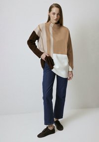 Gehaakte trui in beige, bruin en wit met verticale strepen. Heeft een hoge hals en een oversized pasvorm. Gepaard met een rechte denim.