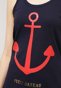 Marinblå linne med ett stort röd ankarmotiv och guldtexten "PETIT BATEAU" längst ner. Tillverkat av mjukt bomullsmaterial.