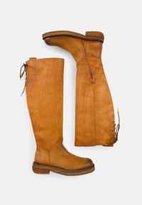 Bottes en cuir tan montantes jusqu'au genou, avec un bout arrondi, une fermeture éclair sur le côté et un détail en lacets le long du mollet. Fini texturé solide, talon en bois empilé.