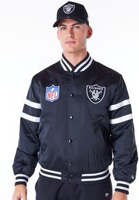 Chaqueta bomber negra con rayas blancas, logotipos de la NFL y de los Raiders. Cuello, puños y dobladillo acanalados. Tejido suave y brillante con forro acolchado.
