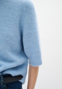Ljusblå fluffig tröja med korta ärmar, med rund halsringning och mjuk textur. I kombination med ett svart bälte och blå denimjeans.