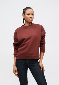 Burgunderfarget genser i mykt stoff, med rund hals, senkede skuldre og ribbestrikkede mansjetter, kombinert med mørke denimbukser.