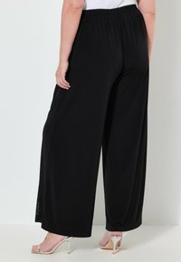 Schwarze weit geschnittene Hose aus weichem Stoff, mit elastischem Bund und seitlichem Schlitz. Kombiniert mit silbernen High-Heels.