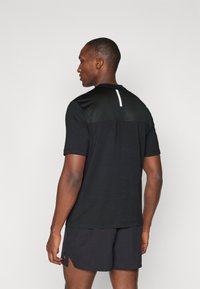 Svart atletisk t-shirt med meshnacke, korta ärmar och en vit accent vid halsringningen. Bärs med matchande svarta shorts.
