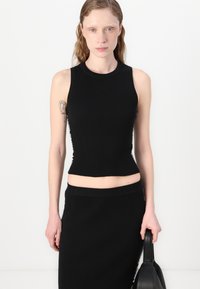 Fekete bordázott kötött crop top kerek nyakkivágással és testhez álló fazonnal, amely egy hozzáillő fekete szoknyával van párosítva. Simább textúrával rendelkezik.
