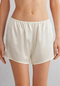 Zijdeachtige, crèmekleurige shorts met een elastische tailleband, met een zachte textuur en een subtiele glans, korter dan de dij met ronde zomen.