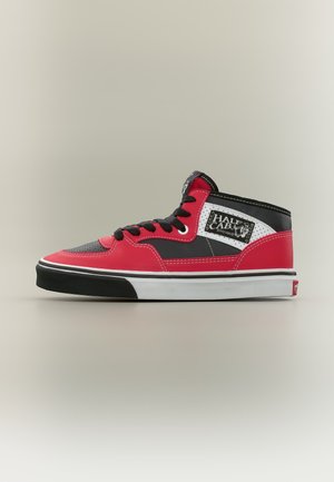 Chaussure de skate rouge, noire et blanche avec des lacets noirs, un design mi-montant, une semelle blanche et un patch « Half Cab » sur le côté, sur fond uni.