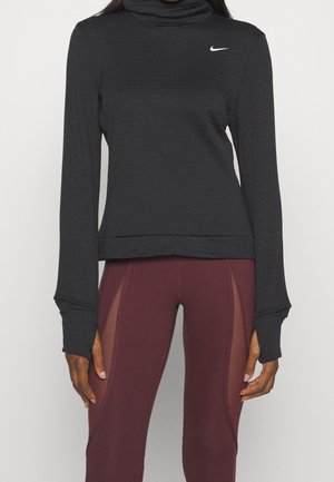 Femme portant un haut Nike noir à manches longues avec passages pour les pouces et des leggings bordeaux avec des panneaux latéraux en mesh.