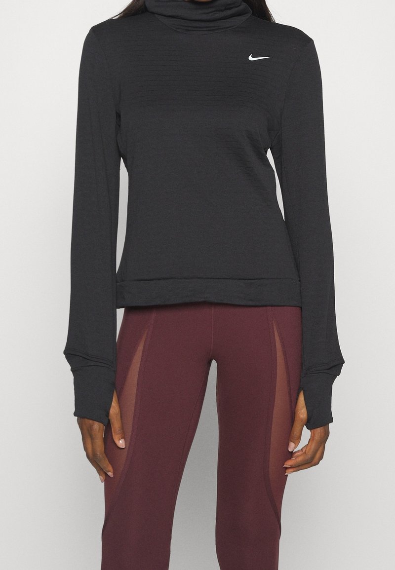 Femme portant un haut Nike noir à manches longues avec passages pour les pouces et des leggings bordeaux avec des panneaux latéraux en mesh.