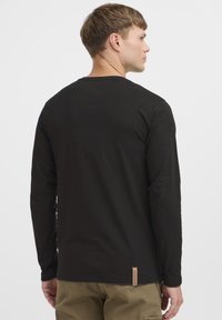 Zwart T-shirt met lange mouwen, van katoen, slim-fit ontwerp, ronde halslijn, zichtbare stiksels, merklabel aan de onderkant aan de linkerkant.