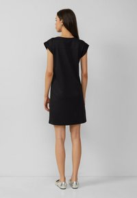 Schwarzes Kurzarmkleid mit lockerer Passform, glatter Textur und rundem Ausschnitt, kombiniert mit metallischen Ballerinas.