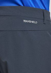 Ciemnoniebieskie spodnie TEXASHIELD o gładkiej, miękkiej teksturze i eleganckim kroju z haftowanym logo na tylnej części pasa.