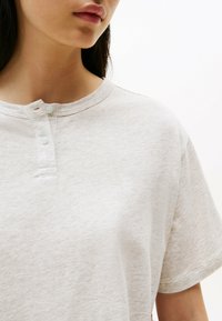 Lysegrå kortærmet skjorte med rund halsudskæring, der har en to-knaps placket og diskret branding. Blødt, struktureret stof.