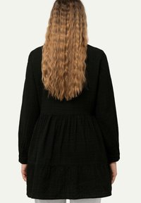 Zwarte, textuurvolle jurk met lange mouwen, geplooide taille en gelaagde zoom, van achter bekeken. Zacht, gekreukt stof, geschikt voor casual draag.