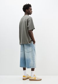 Grå kortærmet t-shirt, løs pasform. Lys blå denimshorts med vide ben, med falmning og logo-detalje. Beige sneakers med gule accenter.