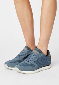 Modré tenisky s texturovanou síťovinou a semišovým materiálem. Zaoblená špička, šněrovací design a kontrastní akcent v oblasti paty.