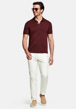Polo bourgogne, pantalon blanc ajusté et chaussures slip-on beige. Le modèle porte des lunettes de soleil, mettant en avant une tenue d'été décontractée.