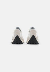 Chaussures de sport avec une tige en suede beige, des accents en cuir blanc, une semelle en caoutchouc noir triangulaire et un col de talon rembourré avec une marque.