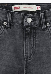 Vaqueros skinny de mezclilla negra con cierre de botón y herrajes plateados, con etiqueta de Levi's y diseño de cinco bolsillos. Talla 12.