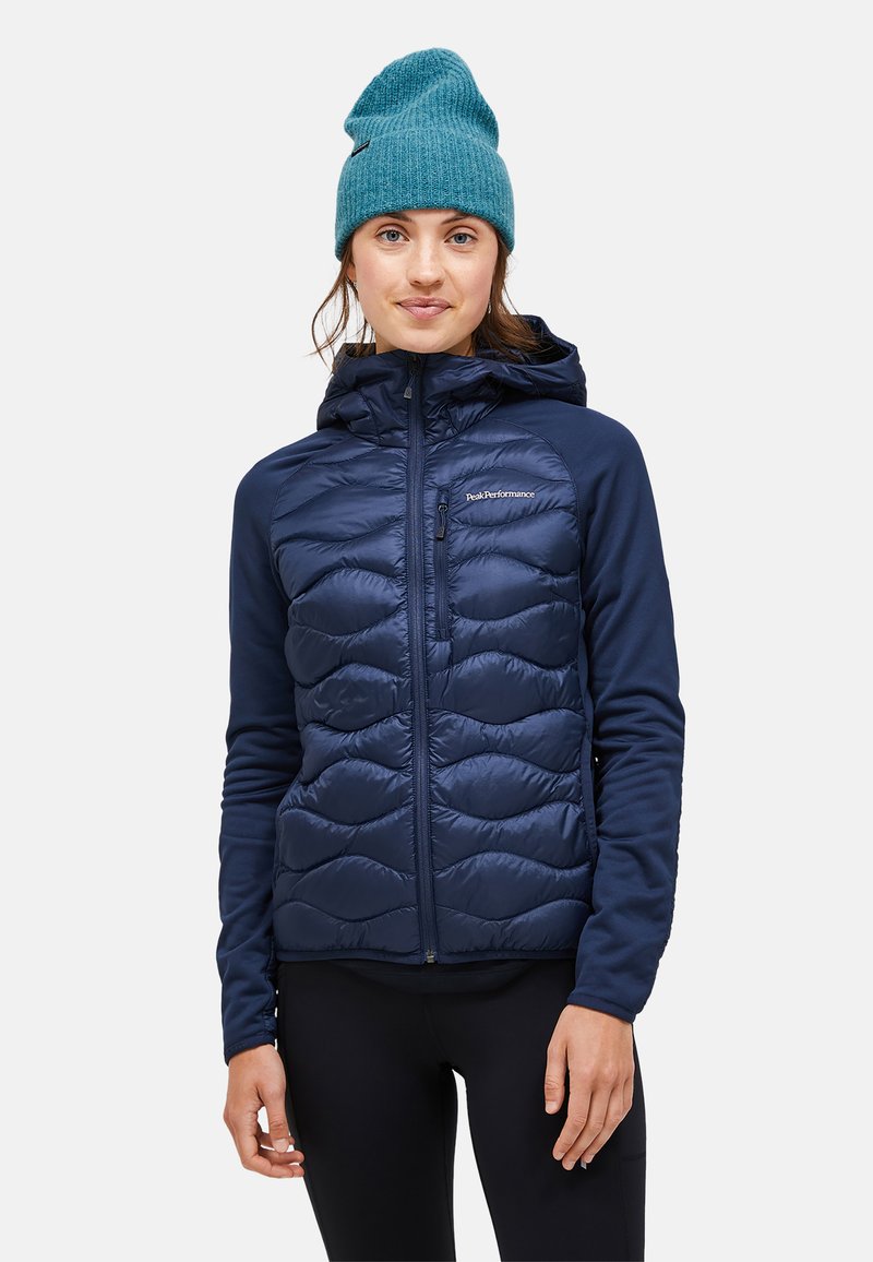 Marineblauer, gepolsterter Jockey mit gestepptem Muster, abnehmbarer Kapuze und Reißverschlusstasche. Weiche Stoffärmel und -körper mit glatter Textur.