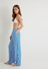 Blauw en wit gestreepte wijde broek met een trekkoord in de taille, voorzien van zijzakken en een relaxte pasvorm. Draag met een witte bikini-top.