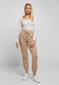 Beige joggebukser med tapered ankler og snøringer. Kombinert med en tettsittende hvit topp med lange ermer. Hvite joggesko fullfører antrekket.