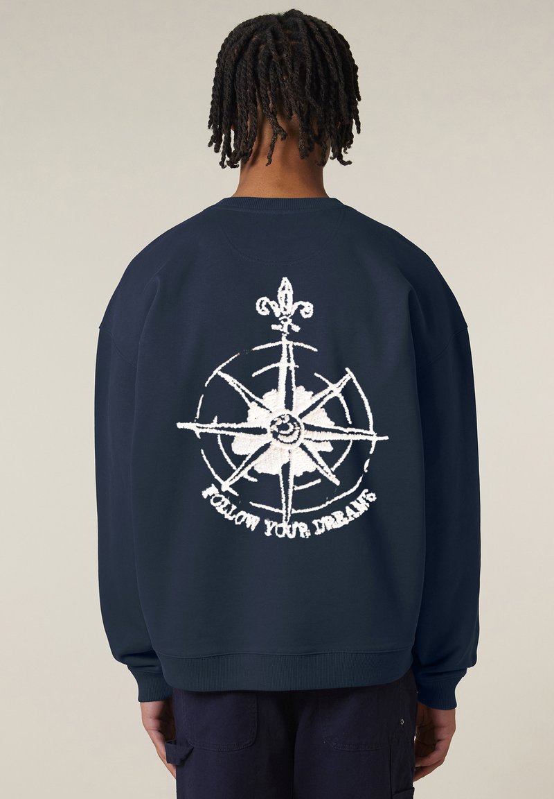 Sweatshirt blu navy con una grande grafica di una bussola bianca sulla schiena con il testo "SEGUI I TUOI SOGNI." Realizzato in tessuto morbido, fit rilassato.