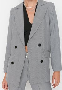 Šedý kostkovaný dvouřadý blazer s klopami, černými knoflíky a texturovanou tkaninou. Vhodný pro formální a smart-casual outfity.