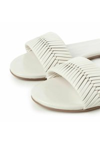 Sandalo bianco con suola piatta e ampia fascia intrecciata. Finitura in pelle liscia con una leggera trama e design a punta arrotondata.