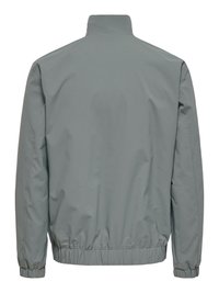 Veste coupe-vent grise avec poignets et ourlet élastiques, montrée de dos avec un col montant et une surface de tissu lisse.