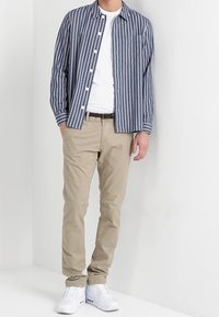 Gestreifte Button-Up-Bluse in Marineblau und Weiß, kombiniert mit beigen Chinos und weißen Sneakers. Das Hemd hat eine Tasche und eine lockere Passform.